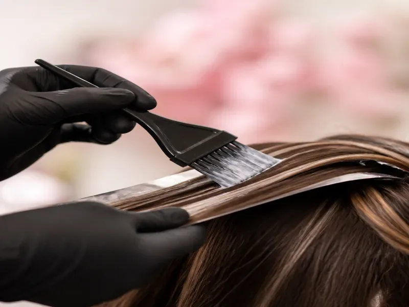 Colorista aplicando balayage con pincel sobre cabello castaño